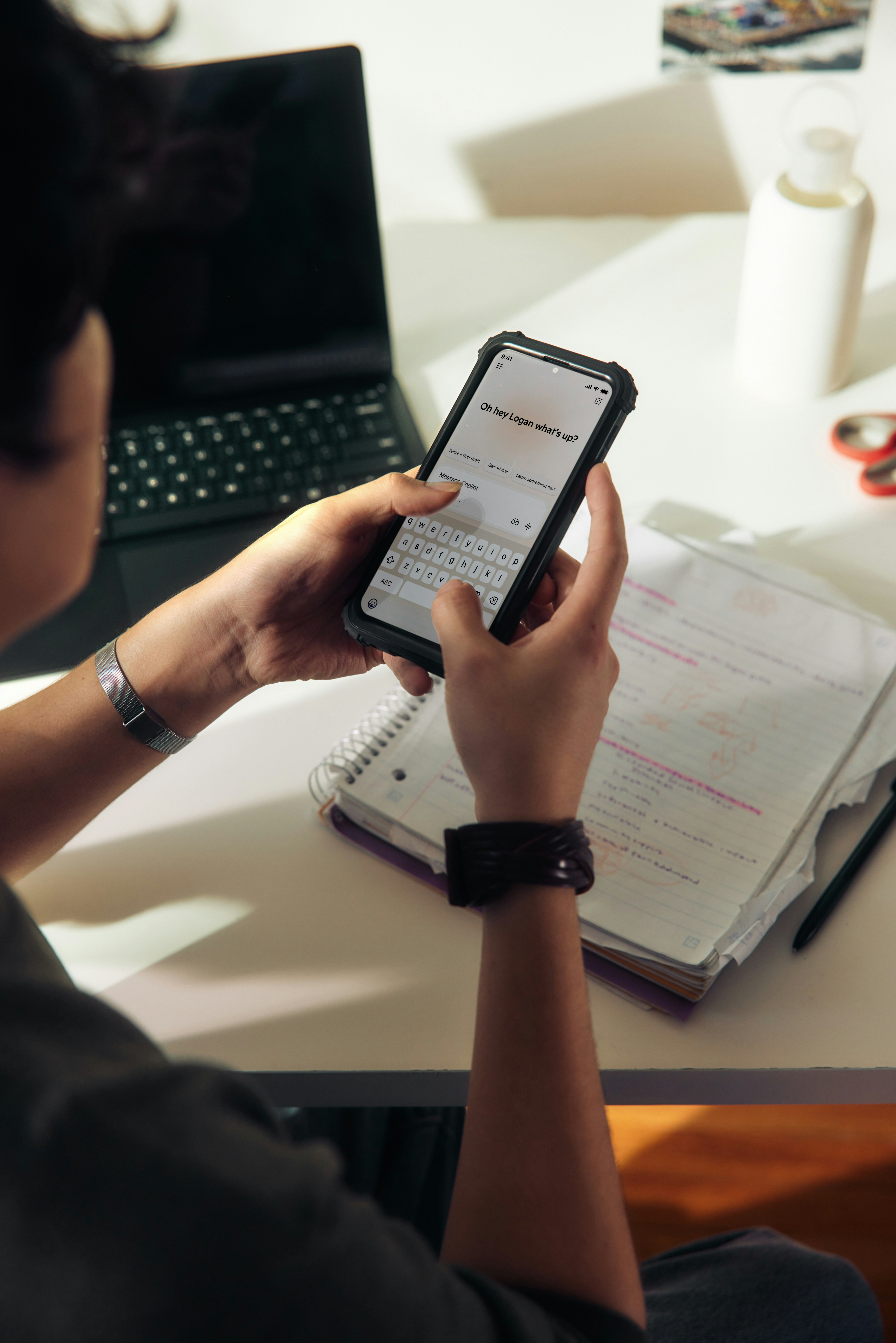 Student on phone at study desk with laptop and notes